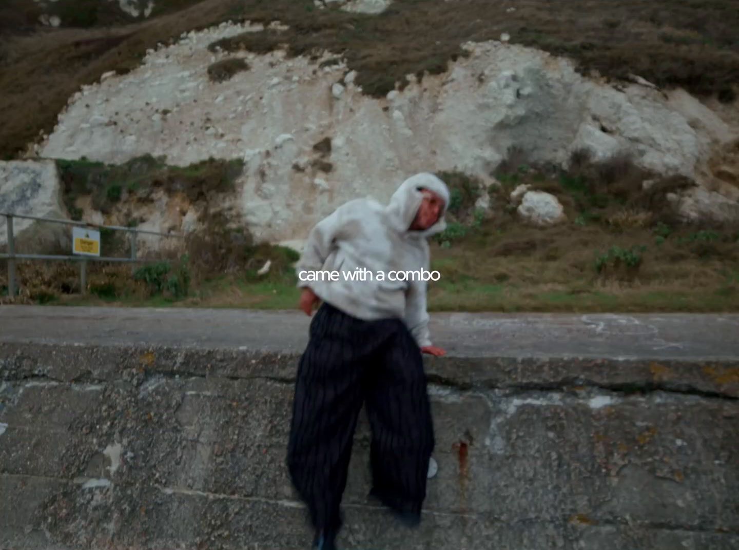 a man in a hoodie leaning against a stone wall