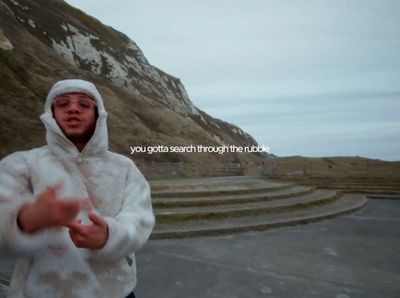 a man in a white hoodie standing in front of a mountain