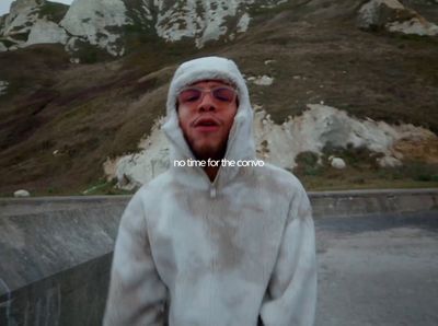 a man wearing a white hoodie standing in front of a mountain