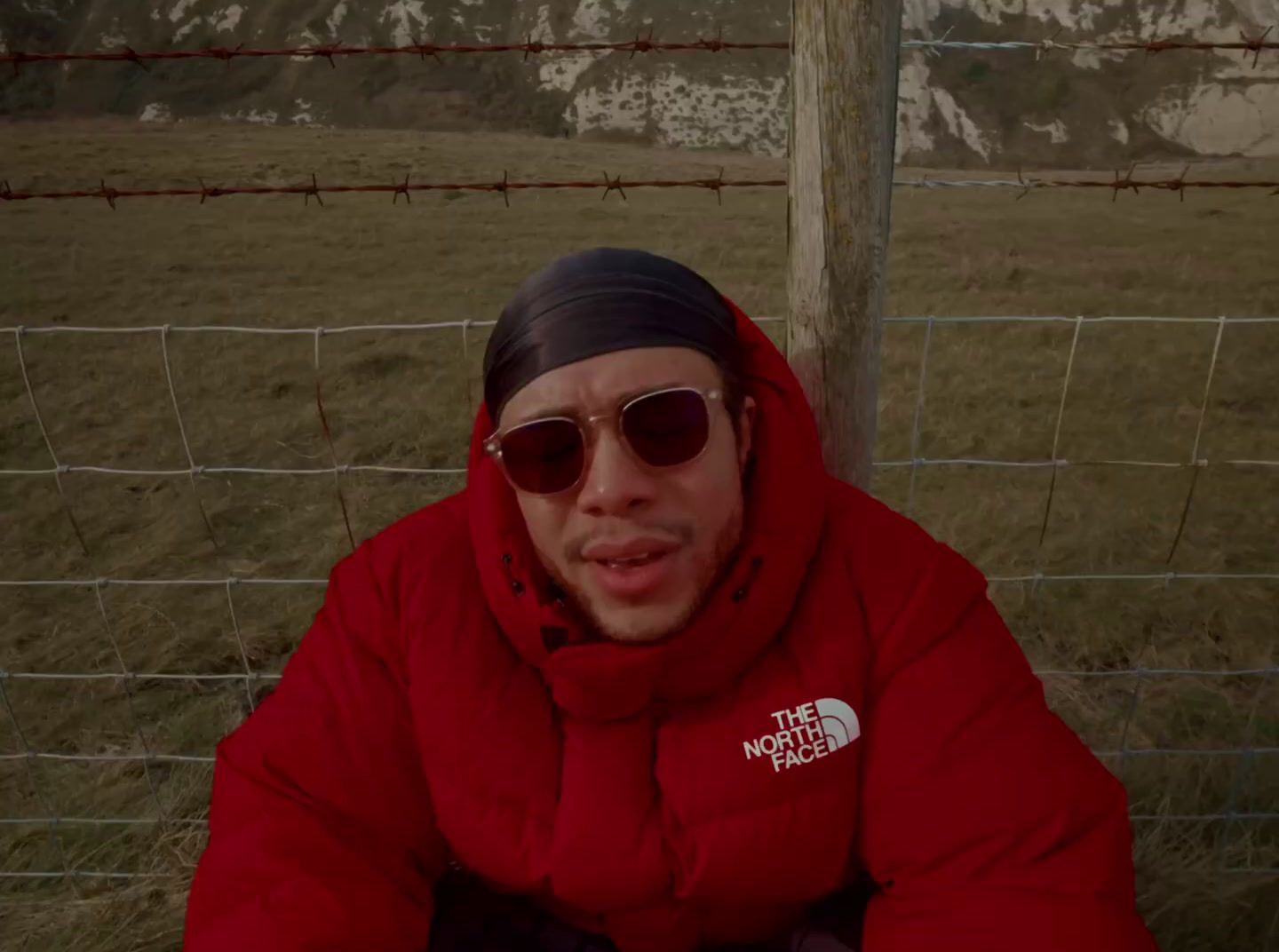 a man in a red jacket sitting in front of a fence