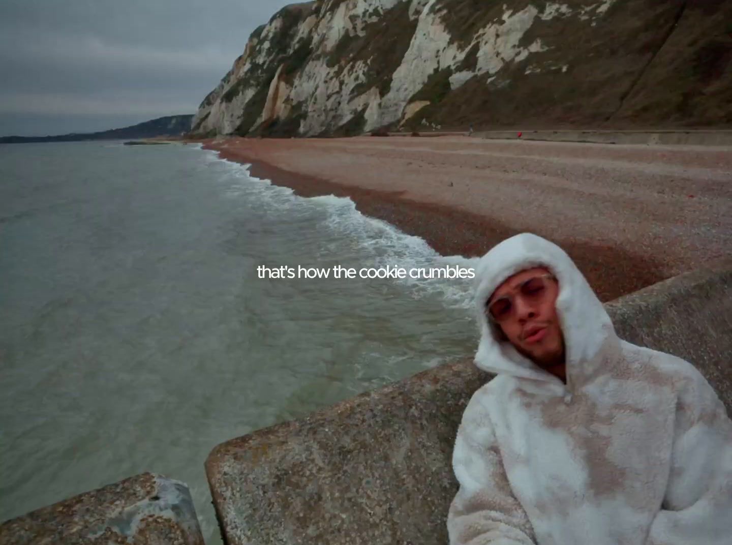 a man wearing a white hooded jacket standing next to the ocean