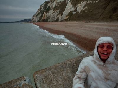 a man in a white jacket standing on a beach next to the ocean