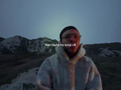 a man in a hooded jacket standing in front of a mountain