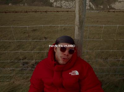 a man in a red jacket sitting in front of a fence