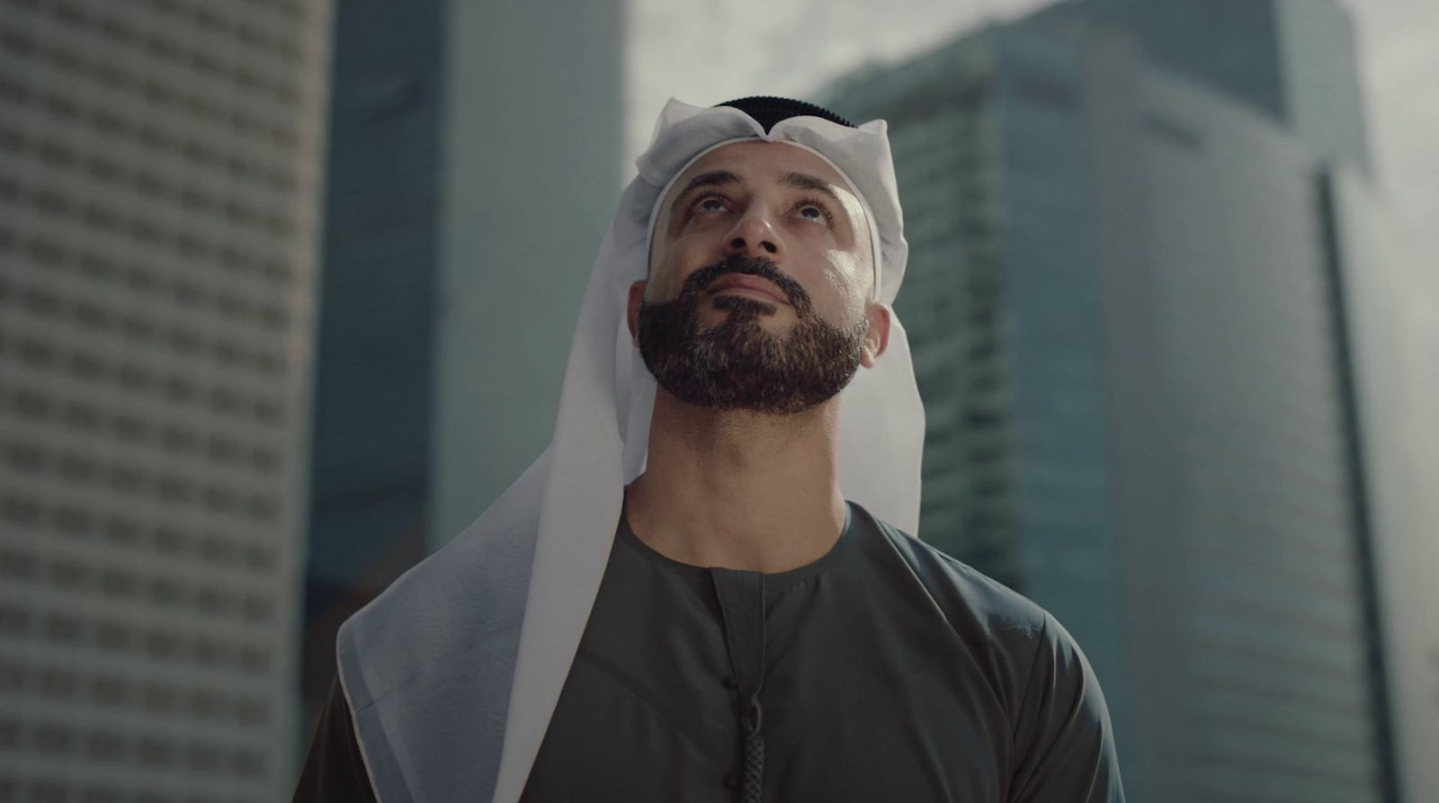 a man wearing a white headdress in front of tall buildings