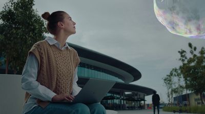 a woman sitting on a bench looking up at a bubble