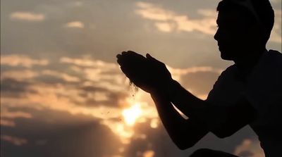 a silhouette of a man praying with the sun in the background