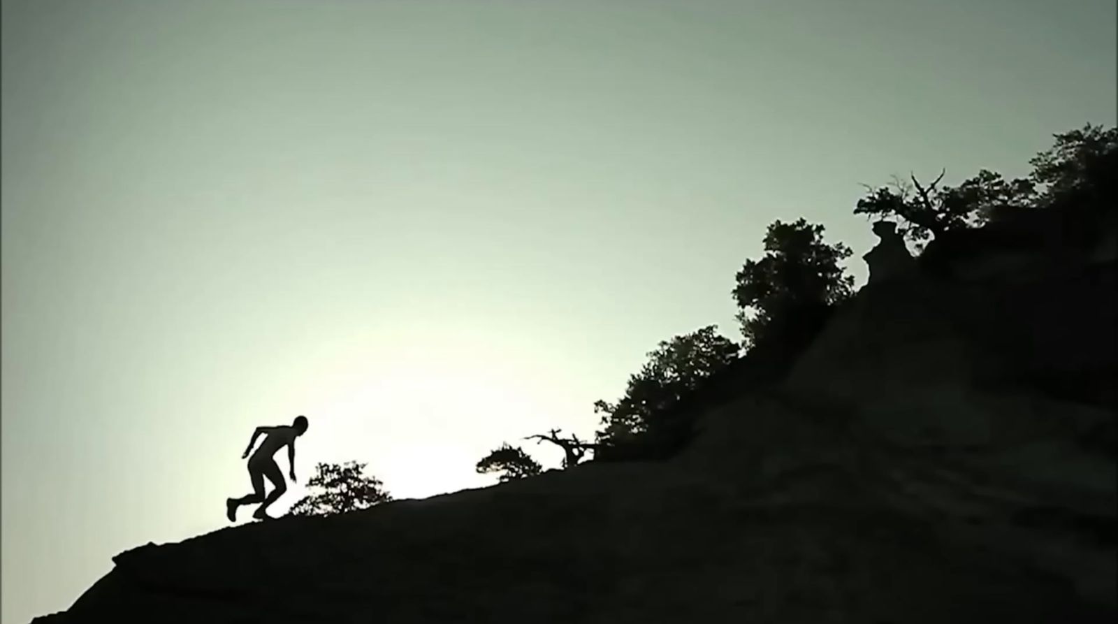 a silhouette of a person jumping off of a cliff