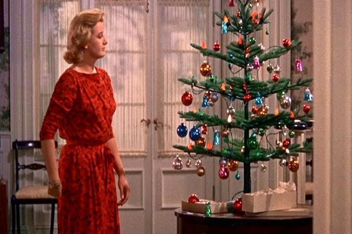 a woman in a red dress standing in front of a christmas tree