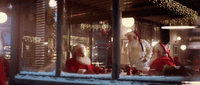 a man and a woman dressed as santa clause looking out a window