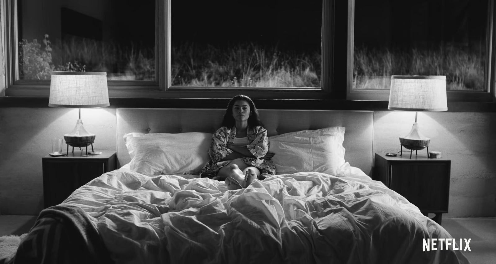 a woman sitting on top of a bed next to two lamps