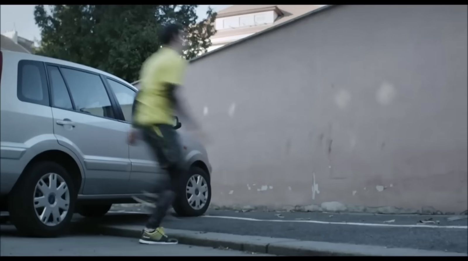 a man in a yellow shirt is walking by a car