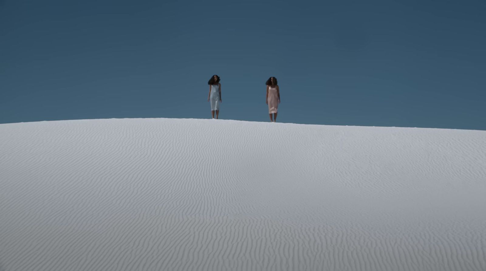 two people standing on top of a white sand dune