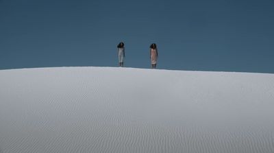 two people standing on top of a white sand dune