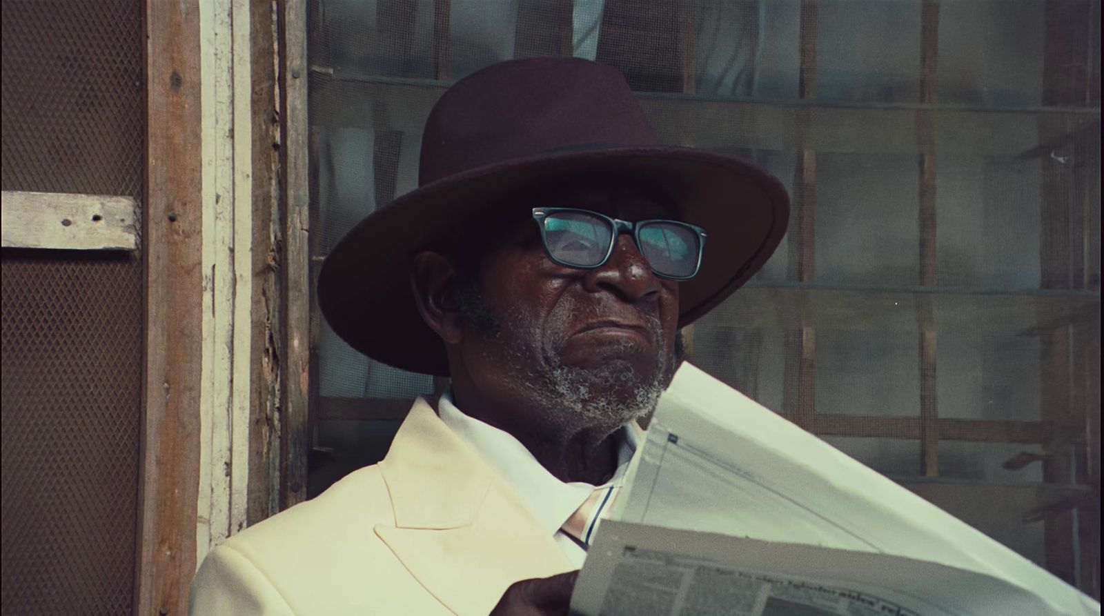 a man in a hat and glasses reading a newspaper