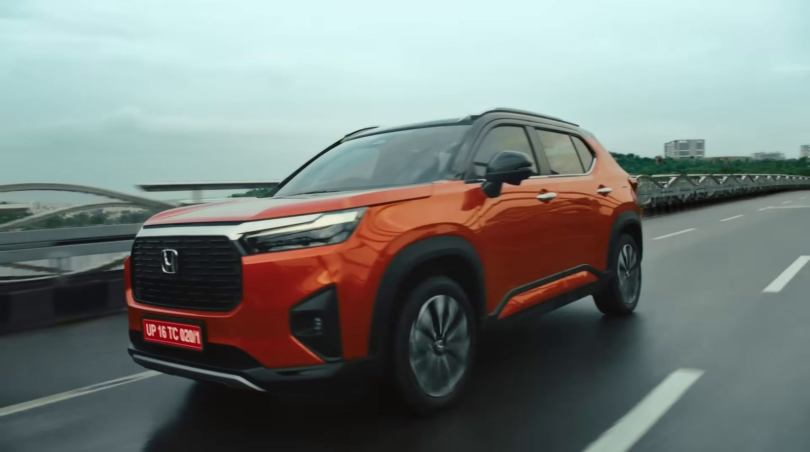 an orange suv driving down a road next to a bridge