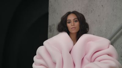 a woman in a pink coat standing next to a wall