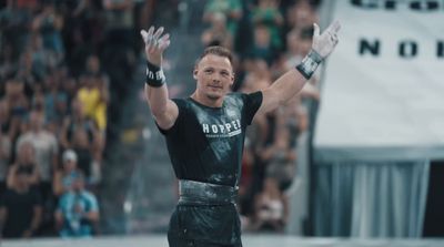 a man in a wrestling outfit raises his hands in the air