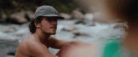 a shirtless man sitting on a rock next to a river