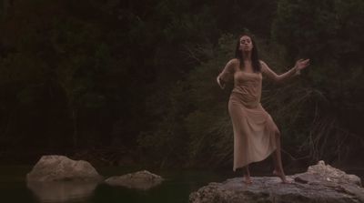 a woman in a dress standing on a rock near a body of water