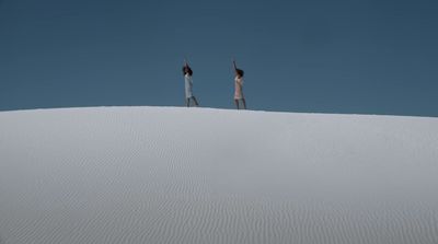 two people standing on top of a white sand dune