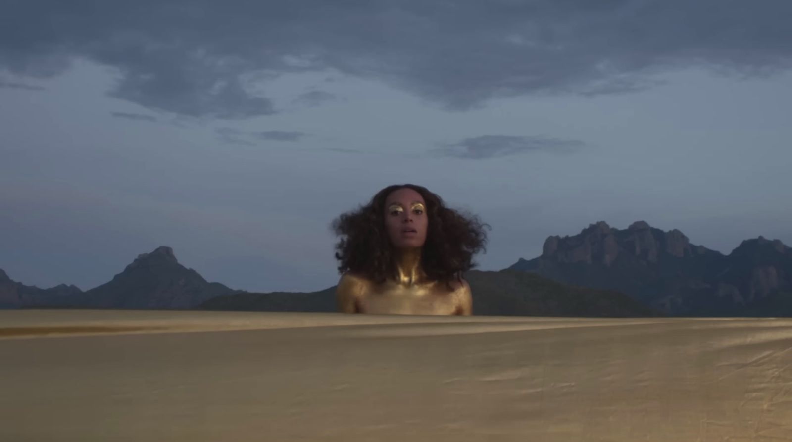 a woman standing in a desert with mountains in the background