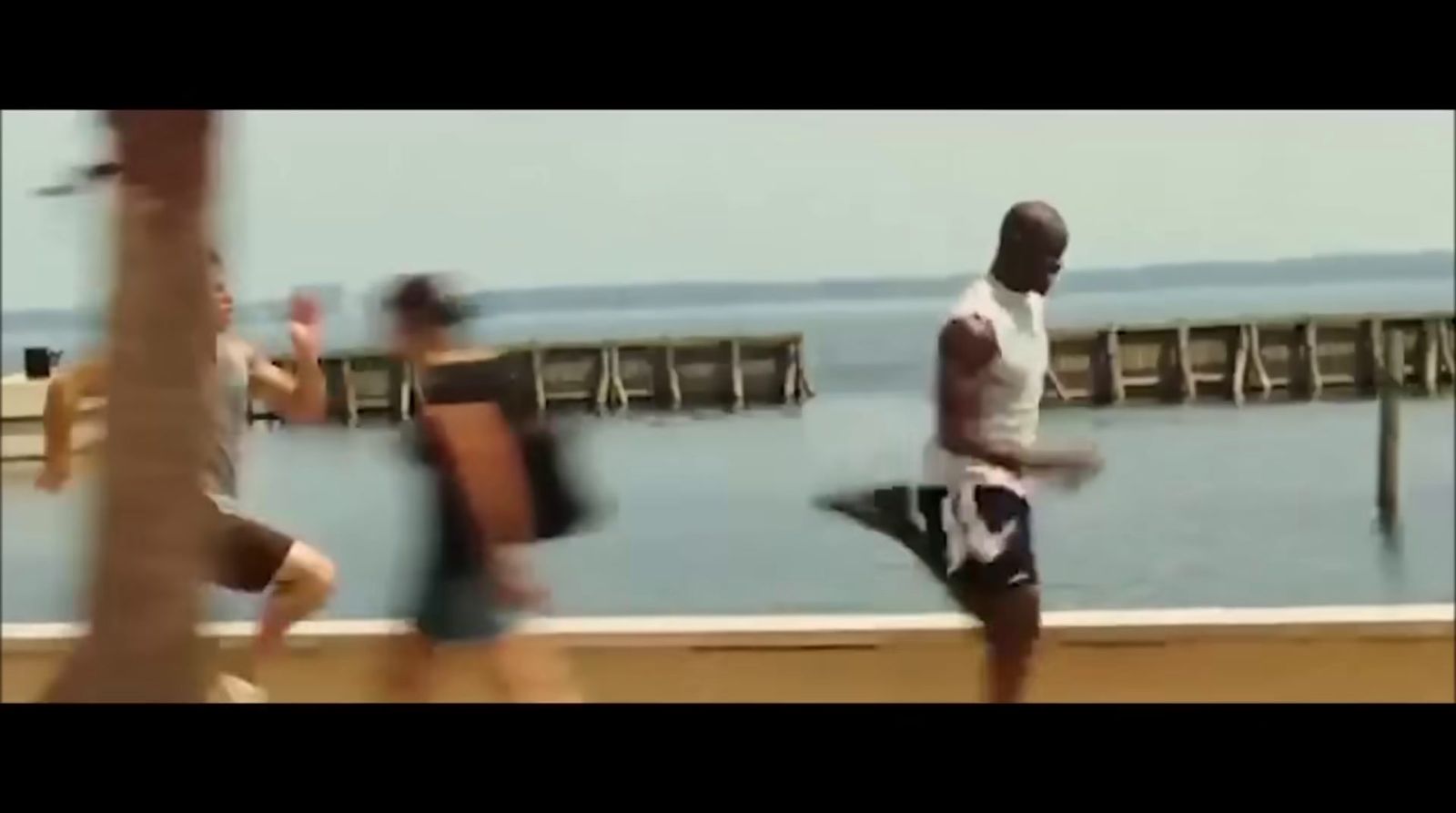 a group of men running along a pier next to the ocean