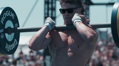 a shirtless man holding a barbell in front of a crowd