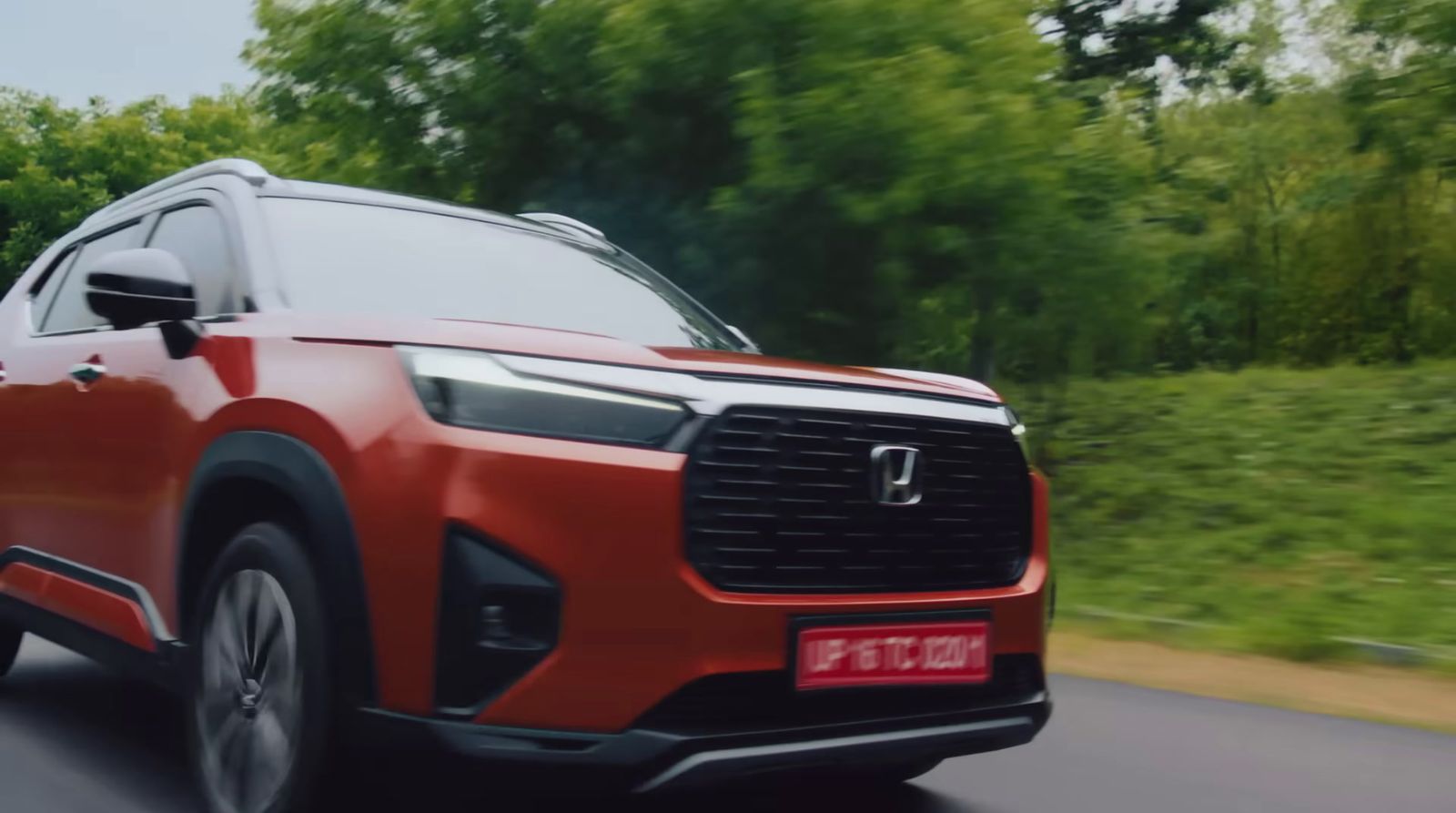 a red suv driving down a road with trees in the background