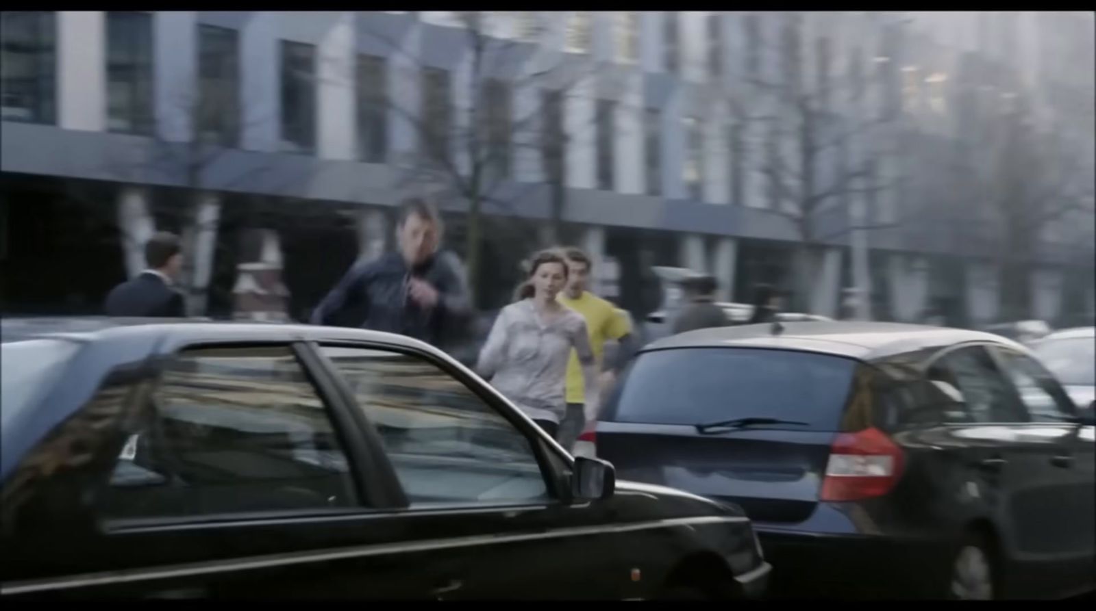 a group of people walking down a street next to parked cars