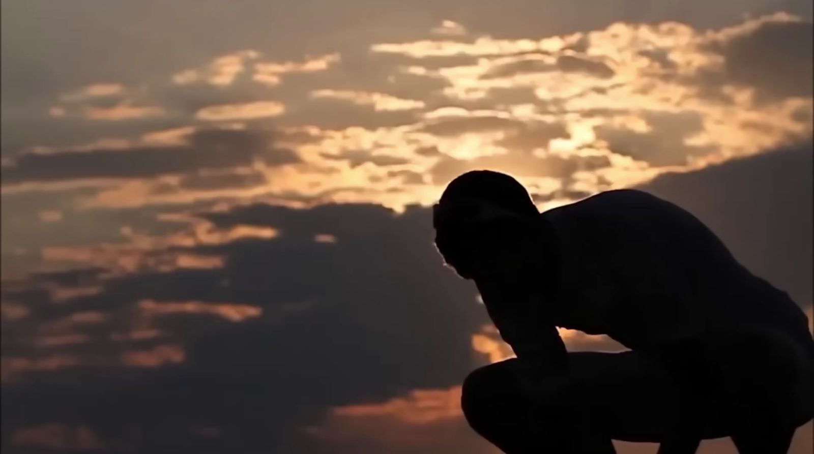 a silhouette of a man crouching in front of a sunset