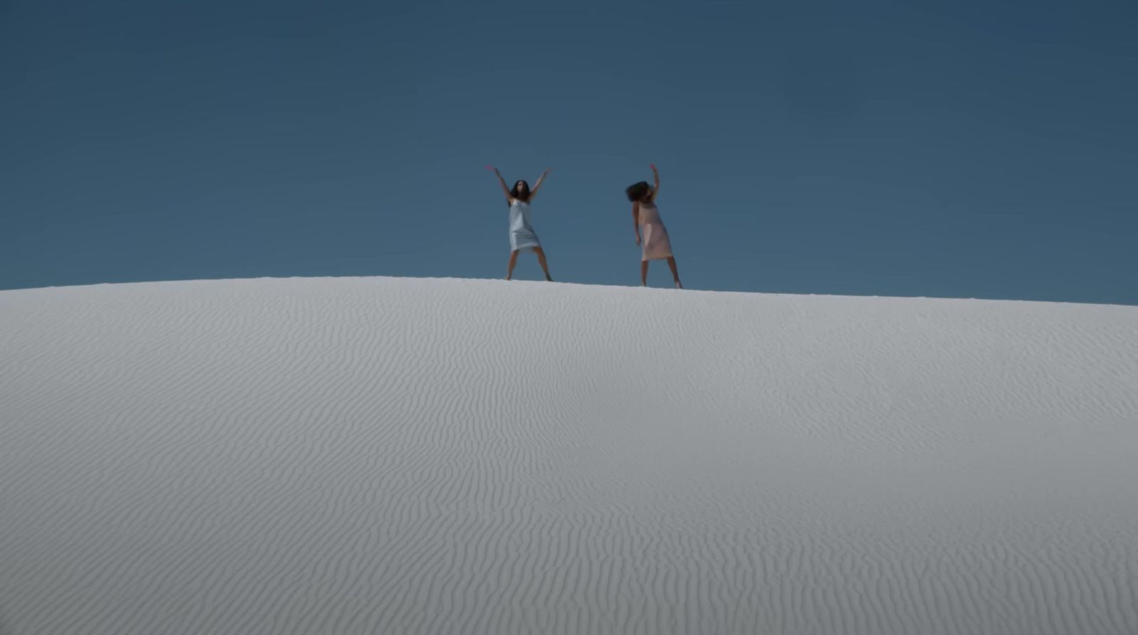 two people standing on top of a sand dune