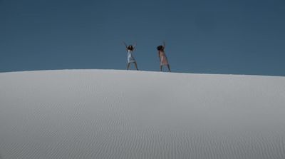 two people standing on top of a sand dune