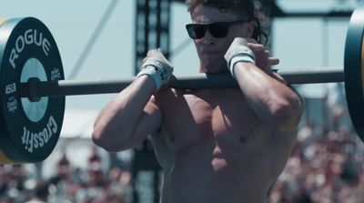 a shirtless man holding a barbell in front of a crowd