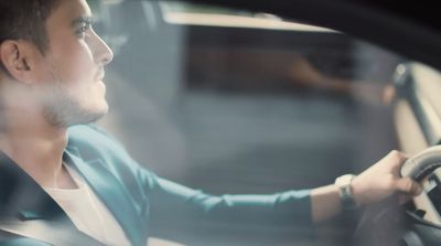 a man driving a car with his hand on the steering wheel