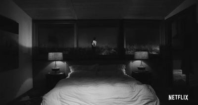 a person standing in a dark room next to a bed