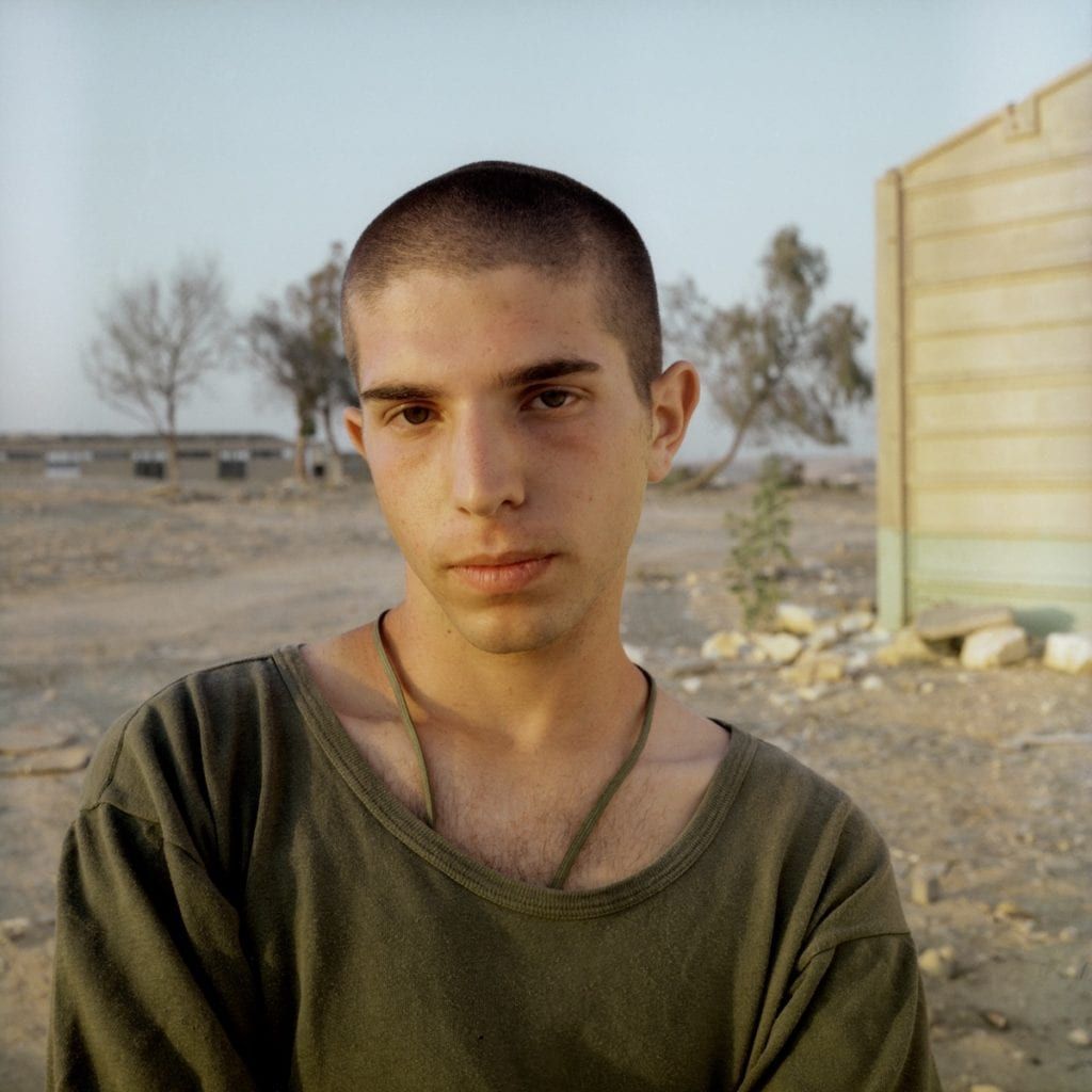 a man standing in a dirt field next to a building