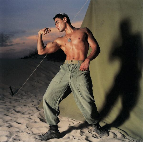a shirtless man poses in the sand