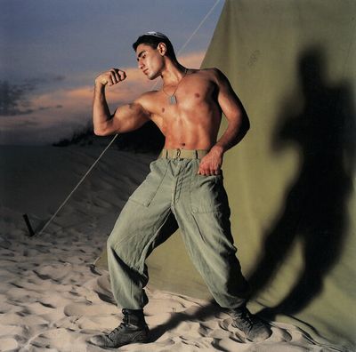 a shirtless man poses in the sand