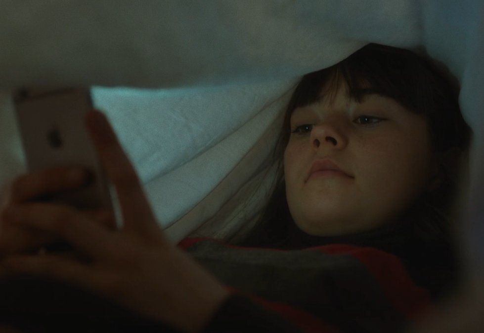 a young girl laying in bed looking at a cell phone