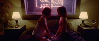 two women sitting on a bed in front of a neon sign