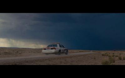 a police car driving down a dirt road under a stormy sky