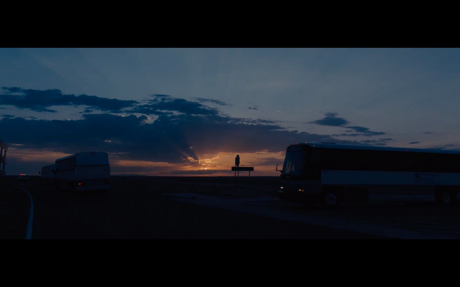 a couple of buses driving down a road under a cloudy sky