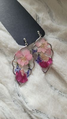 a pair of pink flowers are hanging from a pair of earrings