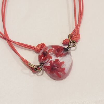a red necklace with a glass heart and flowers