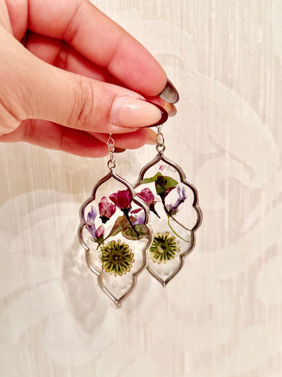 a hand holding a pair of earrings with flowers on them