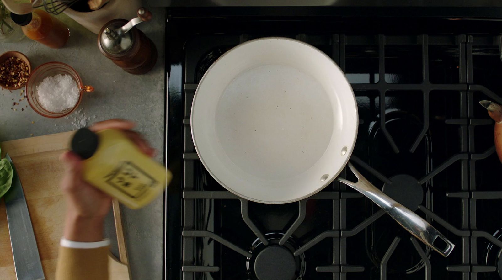 a person holding a bottle of mustard near a pan on a stove