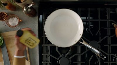 a person holding a bottle of mustard near a pan on a stove