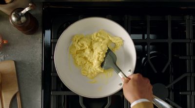 a person using a spatula to mix eggs into a bowl