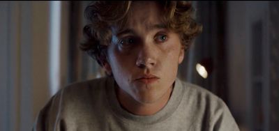 a young man with curly hair stares at the camera